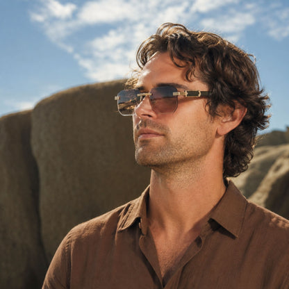 Man wearing rimless sunglasses and a brown shirt.