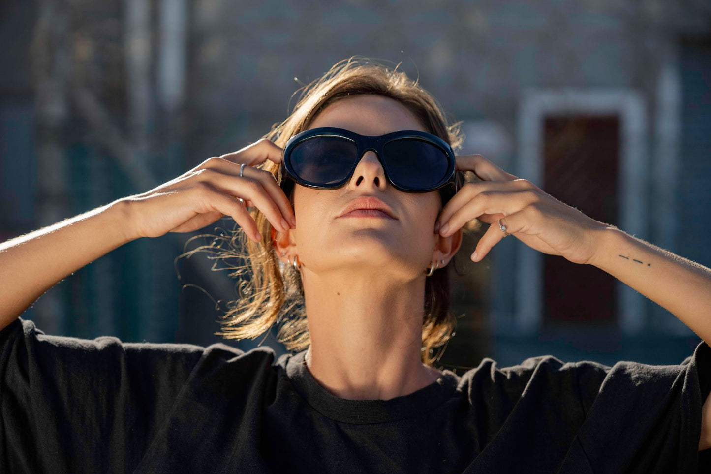 Woman wearing avant-garde party sunglasses with hands framing her face — sculptural oversized cat-eye worn with deliberate editorial confidence, the statement frame that makes every backdrop irrelevant | Sunglass Station