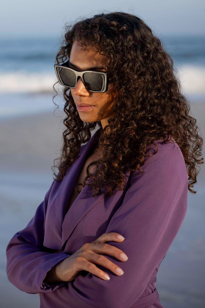 Woman wearing eco bold beach party sunglasses outdoors — effortless sustainable beach style, the thick-frame rectangle cat-eye that elevates every holiday outfit from coastal walk to rooftop dinner | Sunglass Station