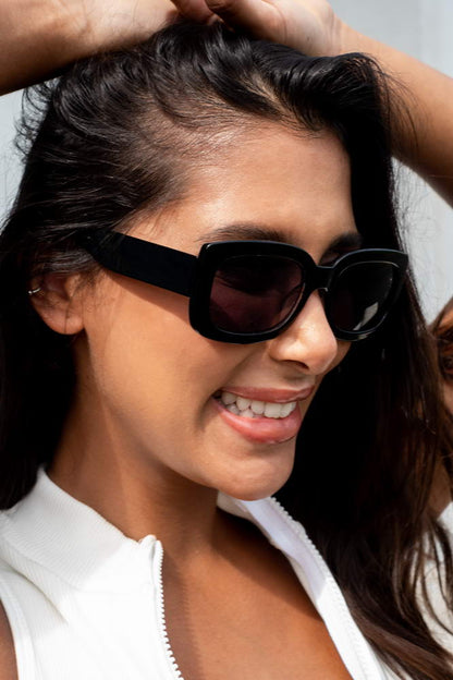 Woman wearing eco bold rectangle party sunglasses — chunky sustainable rectangle worn with effortless confidence, the bold eco frame that moves from city break to festival without asking permission | Sunglass Station