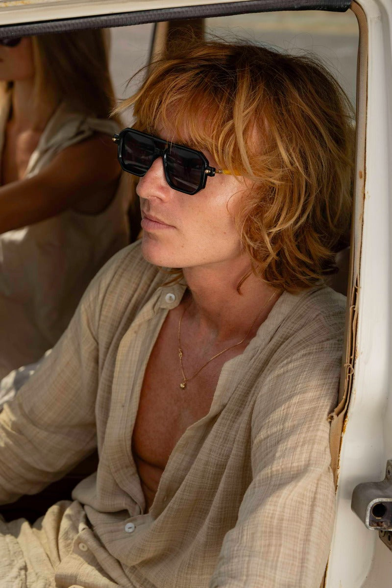 man wearing eco geometric party sunglasses outdoors — effortlessly worn bold navigator frame in recycled polyester, the sustainable eyewear that proves conscious dressing and great style are the same decision | Sunglass Station