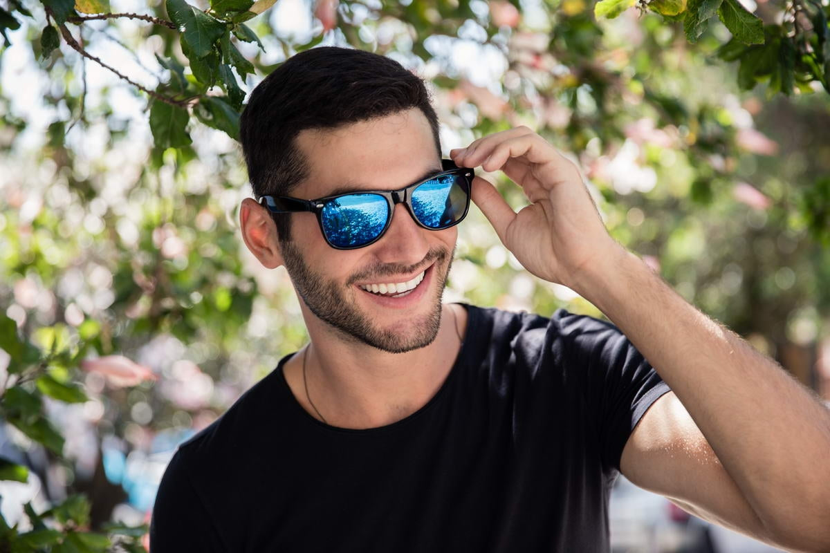 man in blue mirrored wayfarer shades sitting across much river beach