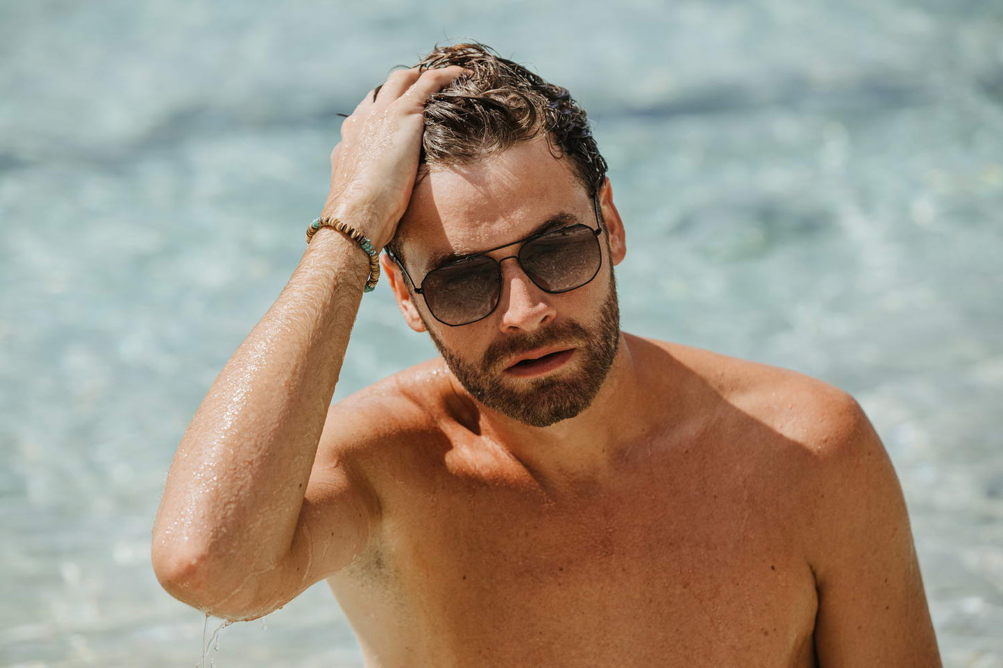 Man wearing modern aviator sunglasses on a beach, perfect for holiday outfits and relaxed outdoor styling