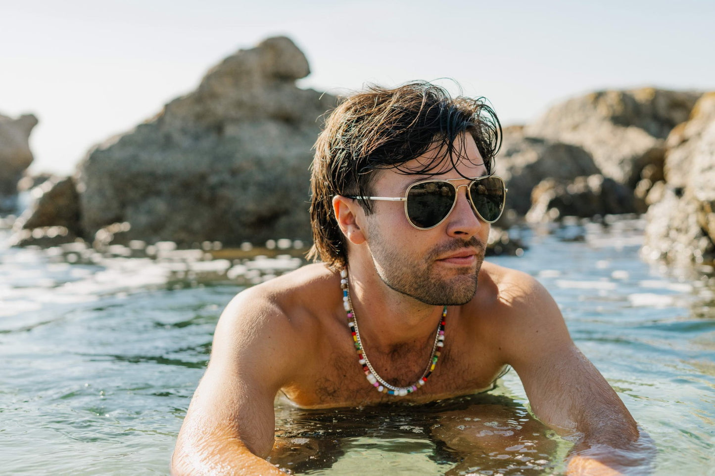 Man wearing aviator sunglasses at seaside location, perfect for beach holidays, travel outfits, and relaxed summer lifestyle styling