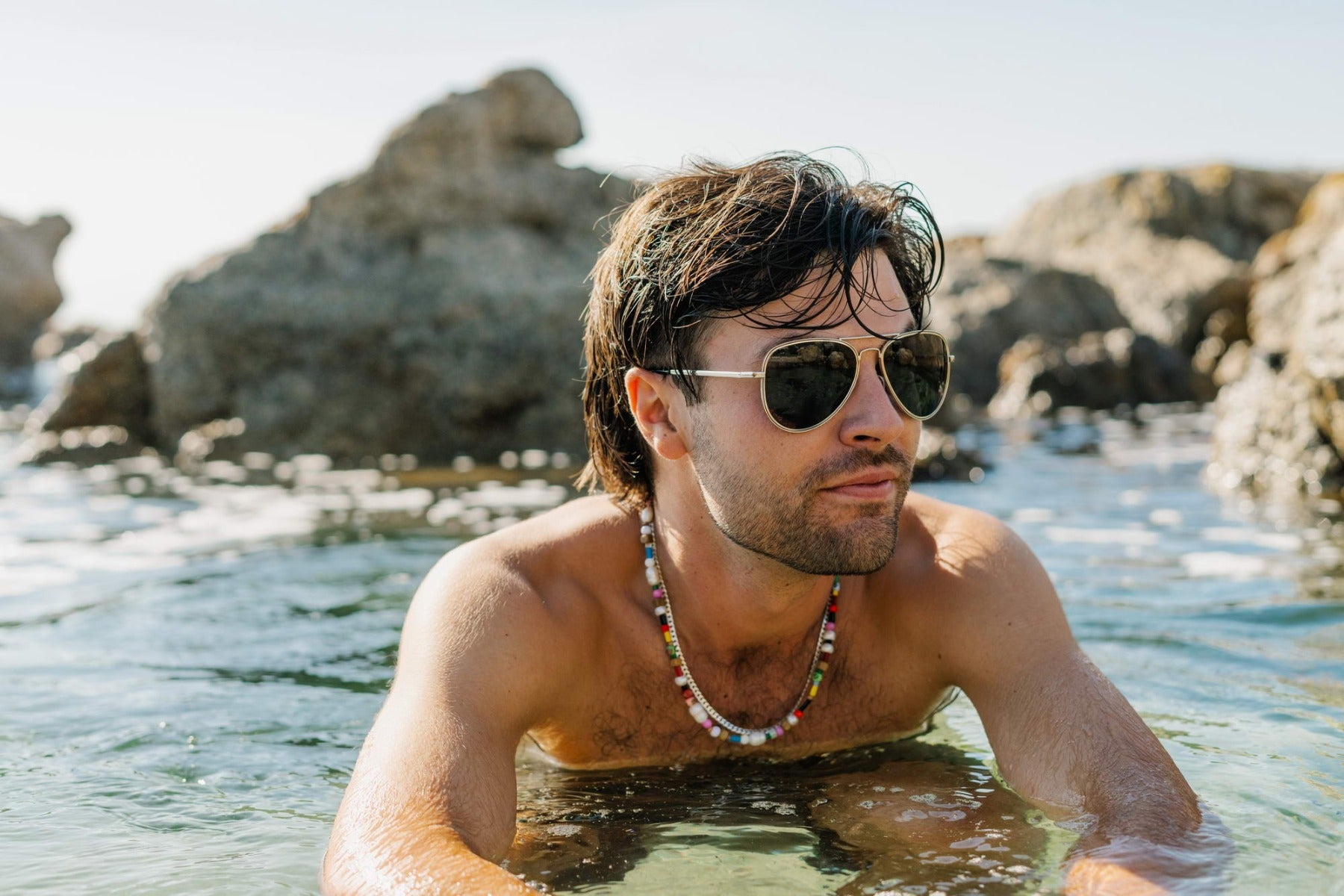 Man wearing aviator sunglasses at seaside location, perfect for beach holidays, travel outfits, and relaxed summer lifestyle styling