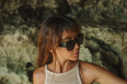 Woman wearing bold cat eye sunglasses outdoors in a natural setting with a relaxed stylish look