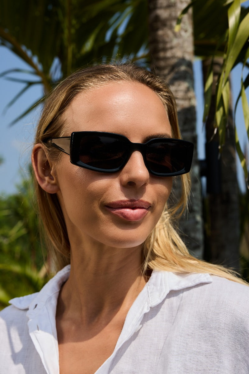 Woman wearing eco black rectangle sunglasses by Sunglass Station, stylish designer eyewear with a sleek modern fit suitable for everyday fashion