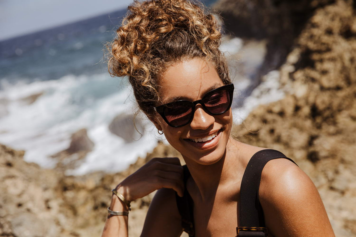 Woman wearing subtle cat eye sunglasses on a beach, featuring lightweight eco frame and soft silhouette ideal for relaxed holiday styling
