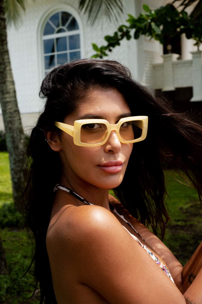Woman wearing yellow rectangle sunglasses by Sunglass Station, stylish unisex eyewear designed for summer outfits and outdoor fashion