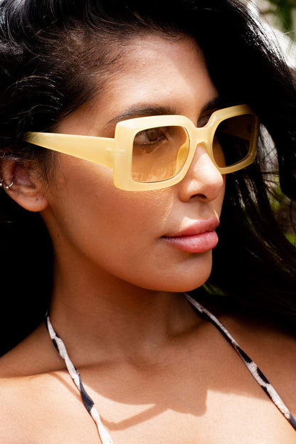 Close-up of yellow rectangle sunglasses worn by a model, bold fashion eyewear by Sunglass Station with lightweight frame and UV protection