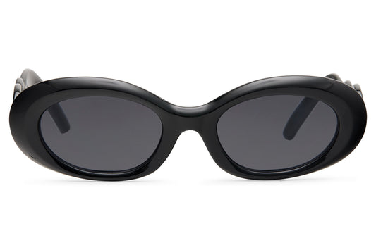 Black chunky oval party sunglasses for women — thick retro frame with deep smoke lens, the silhouette that bridges 90s Saint Laurent and 2026 festival dressing, UV400 recycled polycarbonate